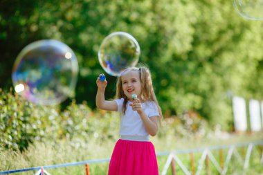 Bir kız yazın parkta sabun köpüğü üflüyor.