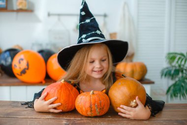 Mutfakta elinde balkabaklarıyla cadı kostümü giymiş küçük bir kız.