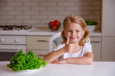 Gülümseyen küçük sarışın mutfakta başparmağını gösteriyor. 