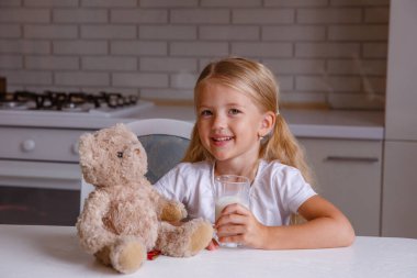 Gülümseyen küçük sarışın kız mutfakta süt içiyor. 