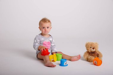 Bebek kız plastik oyuncaklarla oynuyor, stüdyoda oyuncak ayıyla poz veriyor. 