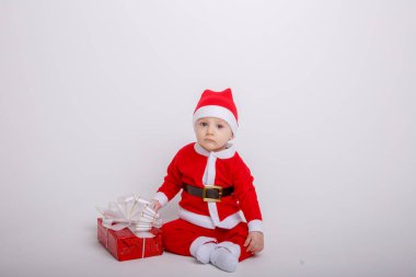 Noel Baba kostümü giyen sevimli çocuk hediye kutusuyla yerde poz veriyor.