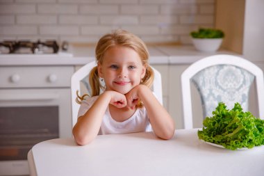 Sarışın bebek mutfakta oturuyor.