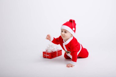 Noel Baba kostümü giyen sevimli çocuk yere hediye kutusuyla poz veriyor.