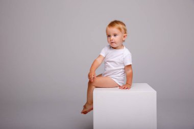 Stüdyoda gri arka planda poz veren küçük kız küpün üzerinde oturuyor 