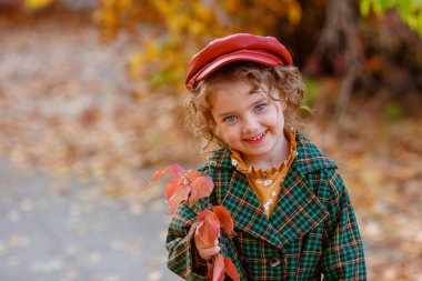 Sonbahar parkında poz veren şık küçük kız. 
