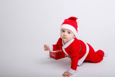 Noel Baba kostümü giyen sevimli çocuk yere hediye kutusuyla poz veriyor.