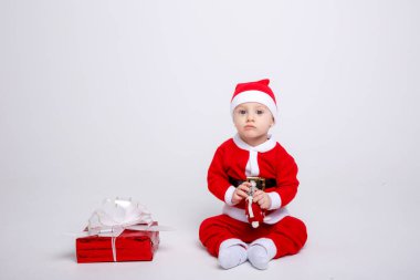 Noel Baba kostümü giyen sevimli çocuk yere hediye kutusuyla poz veriyor.