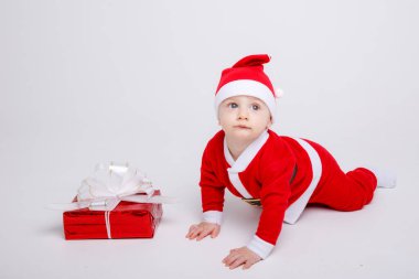 Noel Baba kostümü giyen sevimli çocuk yere hediye kutusuyla poz veriyor.