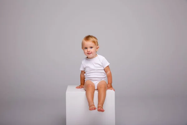 little girl posing in studio against gray background sitting on cube