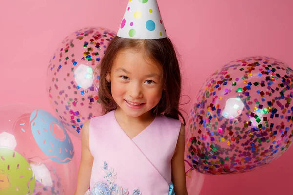 A young Asian girl at a birthday party is playing with balloons on a pink background