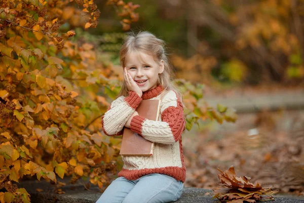 小さなブロンドの女の子で秋に公園で本を持っている — ストック写真