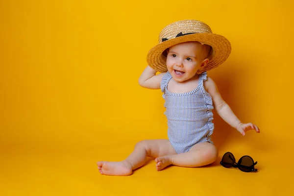 Turuncu Arka Planda Oturan Şapkalı Güneş Gözlüklü Tatlı Küçük Kız — Stok fotoğraf