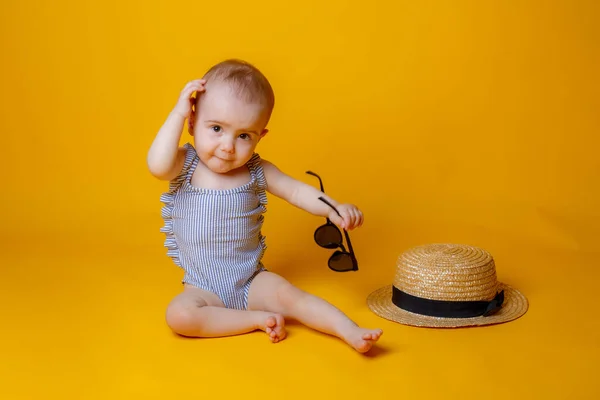 Turuncu Arka Planda Oturan Şapkalı Güneş Gözlüklü Tatlı Küçük Kız — Stok fotoğraf