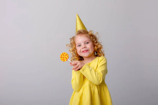 Ένα Κορίτσι Σγουρά Μαλλιά Και Καπέλο Γενεθλίων Κρατώντας Ένα Γλειφιτζούρι — Φωτογραφία Αρχείου