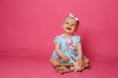 Pembe arka planda oturan elbise giymiş bir kız portresi.