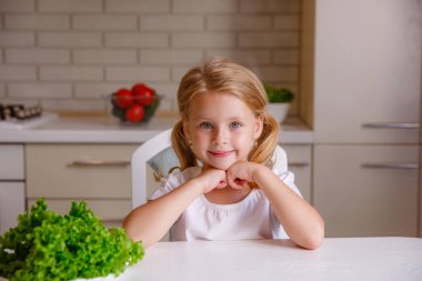 Sarışın bebek mutfakta oturuyor.