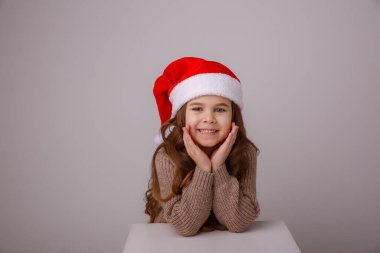 Noel Baba şapkasıyla gri arka planda poz veren tatlı kız.