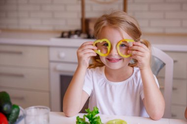 Sarışın bebek mutfakta biberle oynuyor.