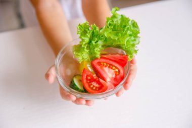 Çocuğun elleri bir tabak sebze tutuyor.