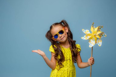 Uzun saçlı küçük bir Asyalı kız mavi arka planda gülümseyen bir yel değirmeni oyuncağı tutuyor.