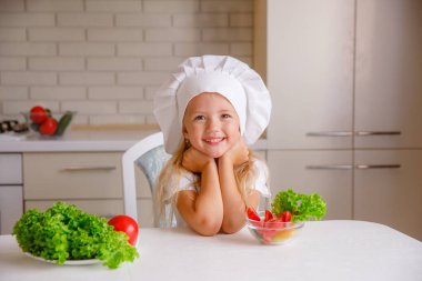 Aşçı şapkası takan sevimli küçük kız yemek yapmaya hazırlanıyor.