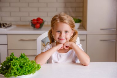 Sarışın bebek mutfakta oturuyor.