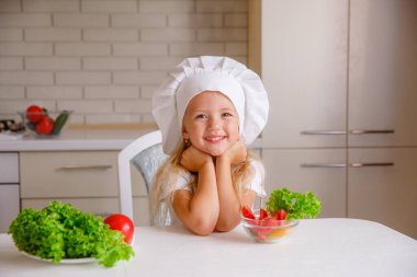 Aşçı şapkası takan sevimli küçük kız yemek yapmaya hazırlanıyor.