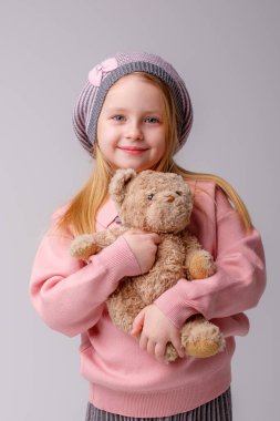 Oyuncak ayıyla gri renge karşı poz veren tatlı kız.