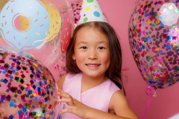 A young Asian girl at a birthday party is playing with balloons on a pink background