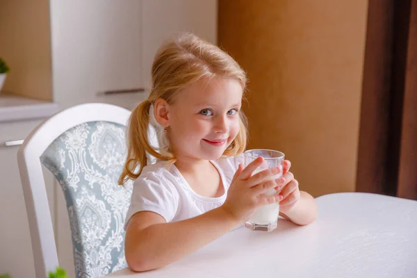 微笑的金发小女孩在厨房里喝牛奶 — 图库照片