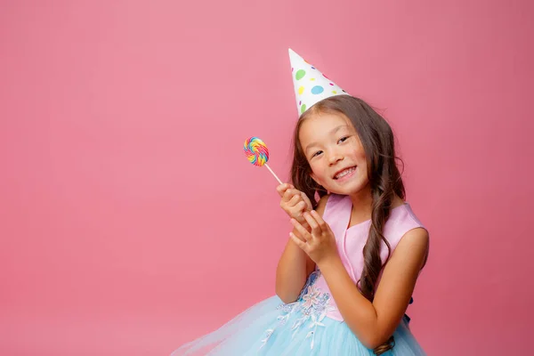 Young Asian girl at a birthday party with a Lollipop on a pink background