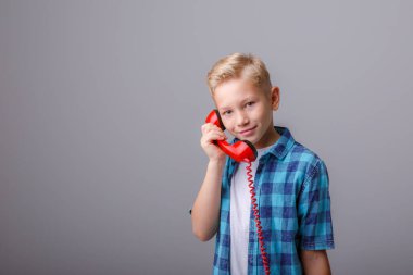 Beyaz tişörtlü, telefon ve gri arka planda siyah tişörtlü bir çocuk.