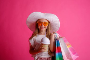 Stüdyoda pembe arka planda bir sürü alışveriş torbası olan küçük bir kız. 