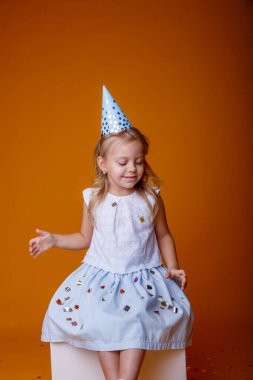 Stüdyoda turuncu arka planda poz veren sevimli doğum günü kızı.
