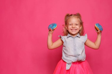 Pembe arka planda donutları olan neşeli küçük bir kız. 