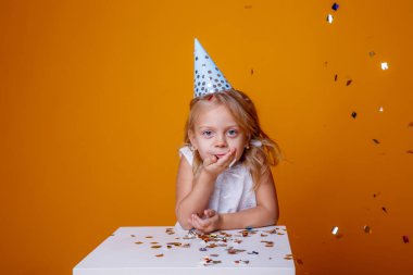 Stüdyoda turuncu arka planda poz veren sevimli doğum günü kızı.