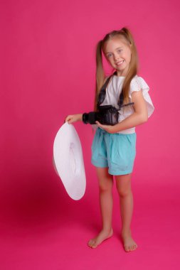 Portrait of a girl traveler, about traveling, holding a camera in her hands in a Studio hat on a pink background clipart