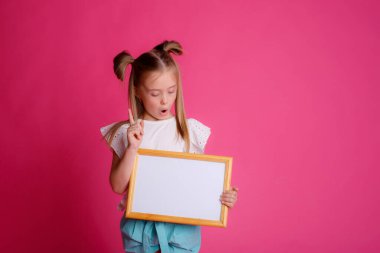 Boş bir çerçeve tutan bir kızın portresi, kareye şaşırmış, pembe arka plandaki metin stüdyosu için yer