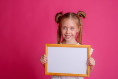 Boş bir çerçeve tutan kız, pembe bir metin stüdyosuna bakıyor.