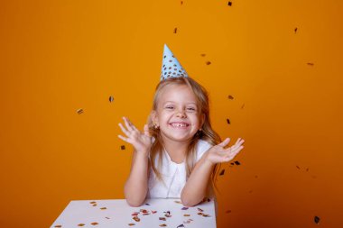 Stüdyoda turuncu arka planda poz veren sevimli doğum günü kızı.