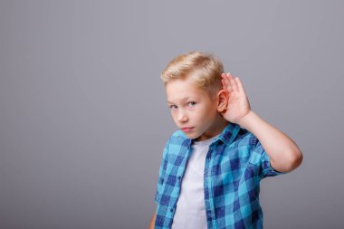 Gömlekli, beyaz tişörtlü, ciddi yüzlü küçük bir çocuk.