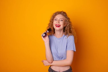 Turuncu arka planda güneş gözlüklü kıvırcık saçlı kadın poz veriyor.