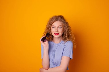 Turuncu arka planda güneş gözlüklü kıvırcık saçlı kadın poz veriyor.