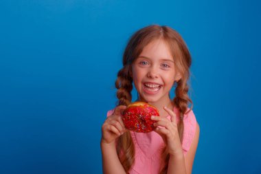 Mavi arka planda donutla poz veren küçük bir kız. 