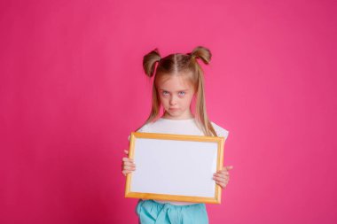 Pembe arka planda boş bir kağıt parçası tutan uzun saçlı küçük bir kız.