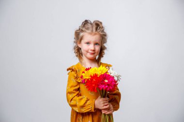 Gri arka planda bir buket çiçekle sarı elbiseli şirin küçük bir kızın portresi.