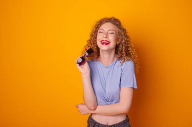 Turuncu arka planda güneş gözlüklü kıvırcık saçlı kadın poz veriyor.