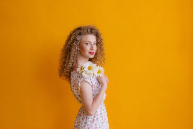 Turuncu arka planda bir buket papatya tutan kıvırcık bir kadın. 