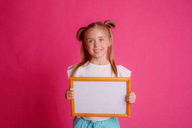 Boş bir çerçeve tutan bir kızın portresi, pembe arka planda metin stüdyosu için gülümseme yeri